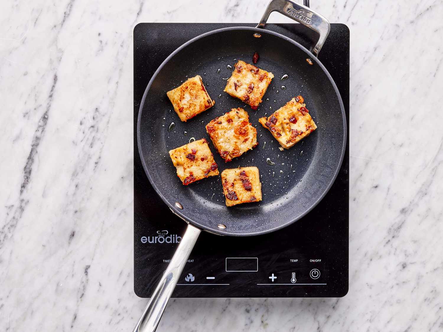 Overhead view of turnip cakes being fried in a pan 