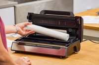 A person places a plastic bag roll into the Nesco VS-12 Deluxe Vacuum Sealer