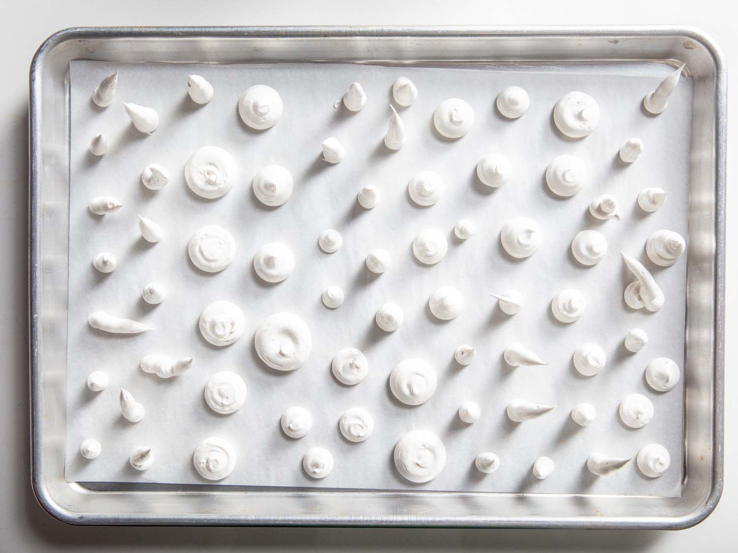 A tray of unbaked meringue mushroom caps and stems, with a glossy white appearance