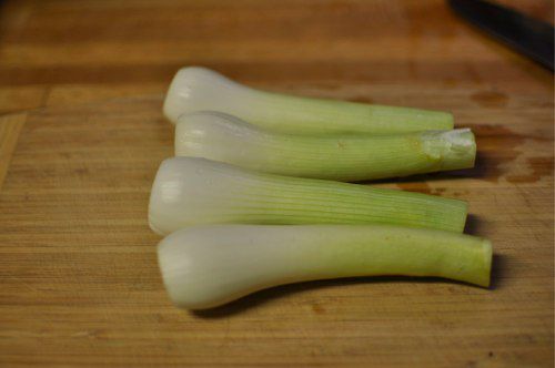 Four spring onions on a cutting board, trimmed and peeled.