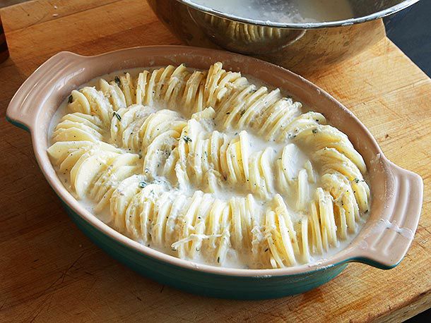 Baking dish with potato slices on their side, coated in cream and cheese, for Hasselback potato gratin.