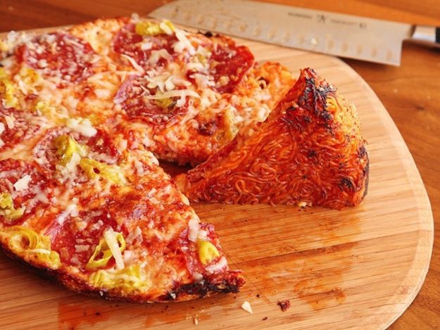A slice of ramen crust pizza is turned on its side to reveal the browned bottom crust.