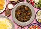 Overhead of Khoresh E Ghormeh Sabzi surrounded with rice, dips, and vegetables 