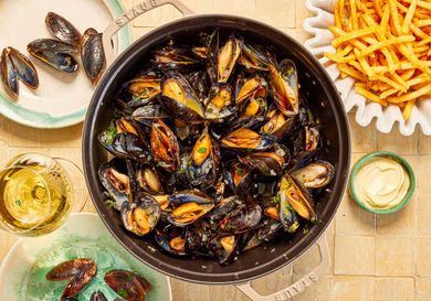 Mussles in a grey Staub Dutch oven and a side of fries.