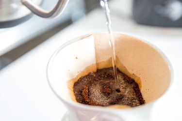 A goose-neck kettle is used to precisely wet coffee grounds, or "bloom" them, before brewing.