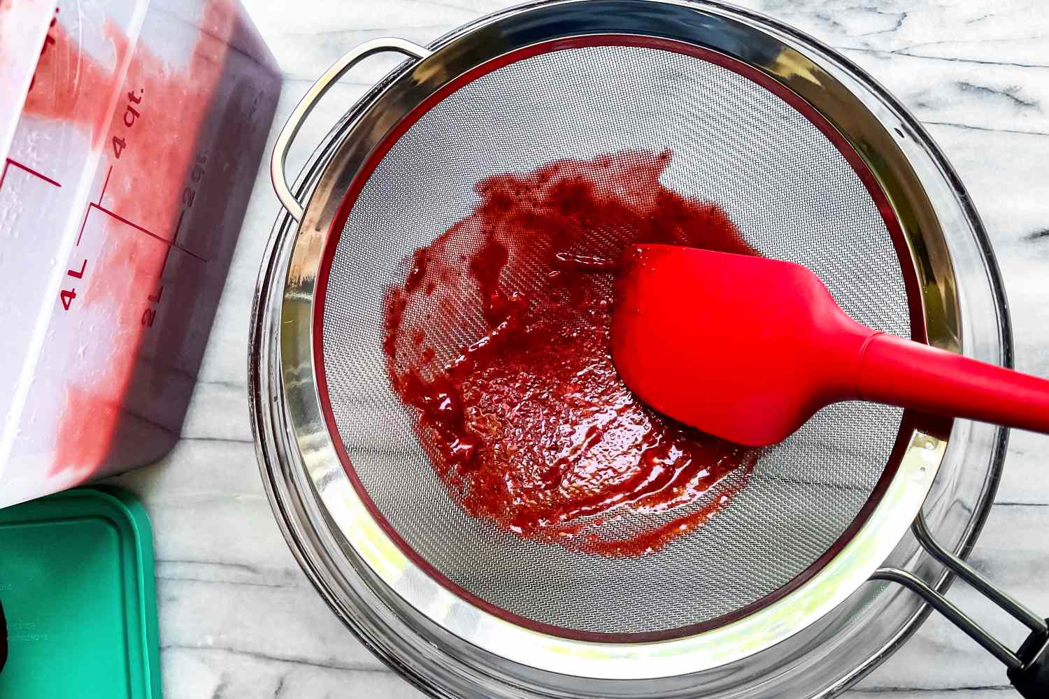 OXO Good Grips 8-Inch Double Rod Strainer with red fruit puree being pressed through using a spatula surrounded by containers