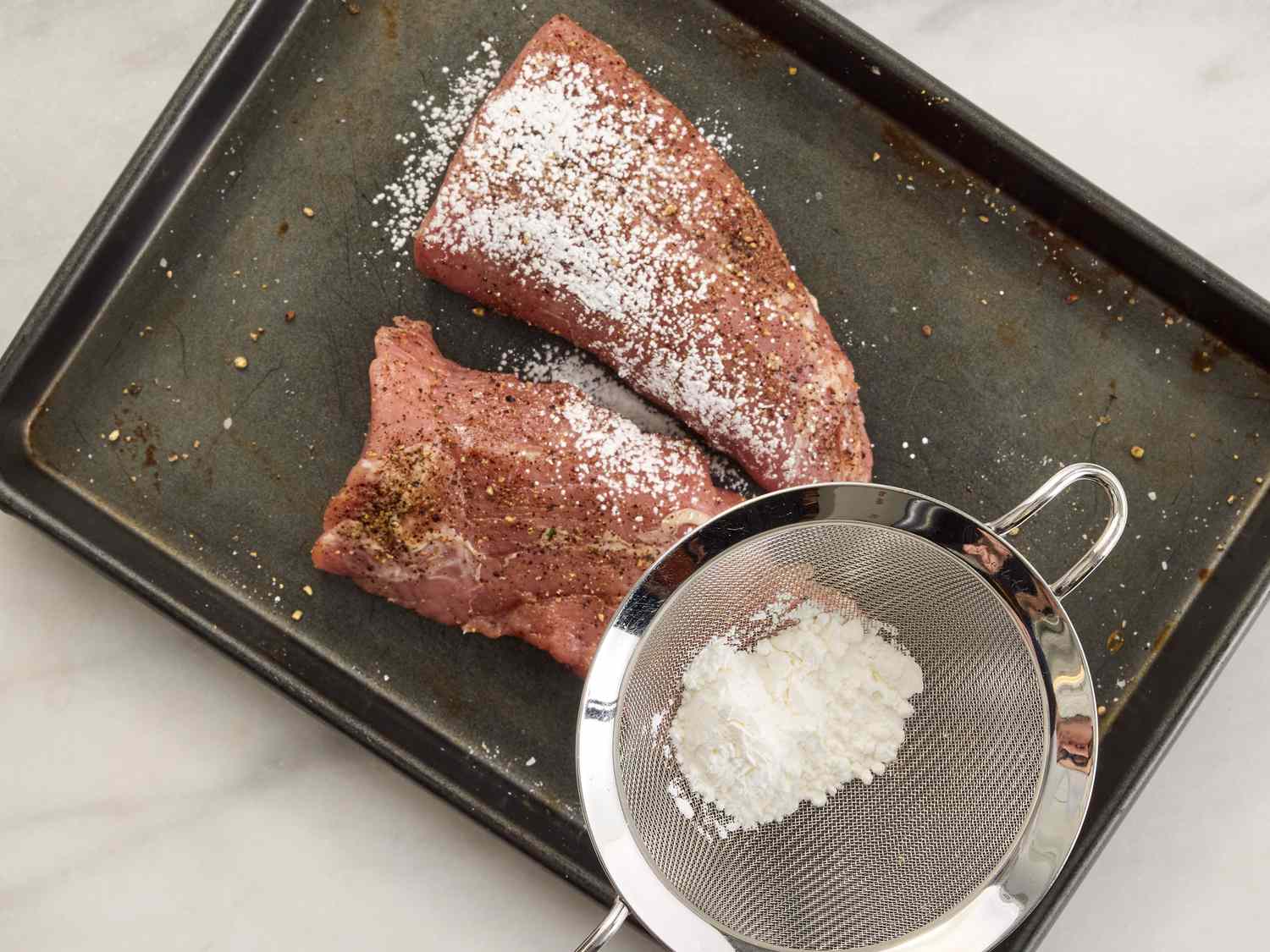 pork on a sheetpan being dusted with cornstarch 