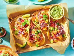 Overhead view of four Baja fish tacos on a parchment-lined tray with guacamole and lime