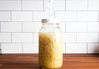 A jar full of sauerkraut on a countertop, with an airlock fixed on top to let gas out.