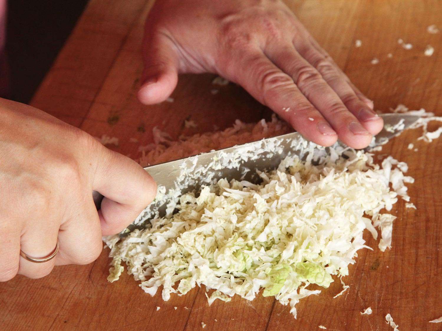 Mincing finely shredded Napa cabbage with a chef's knife on a wood cutting board. 