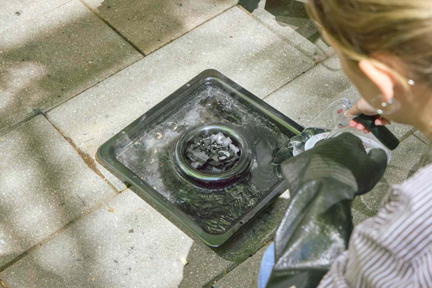 A person adds water to a burner on the Cuisinart COS-244 Vertical 36-inch Propane Smoker