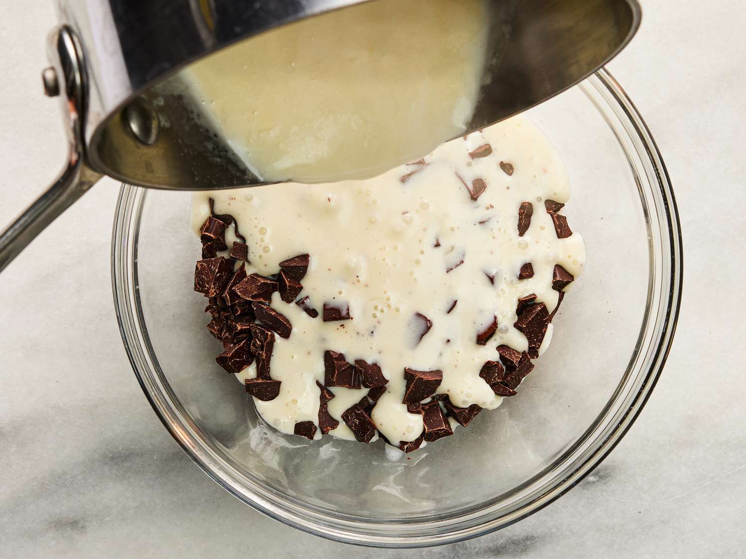 Pouring heavy whipping cream into chocolate in a glass bowl 