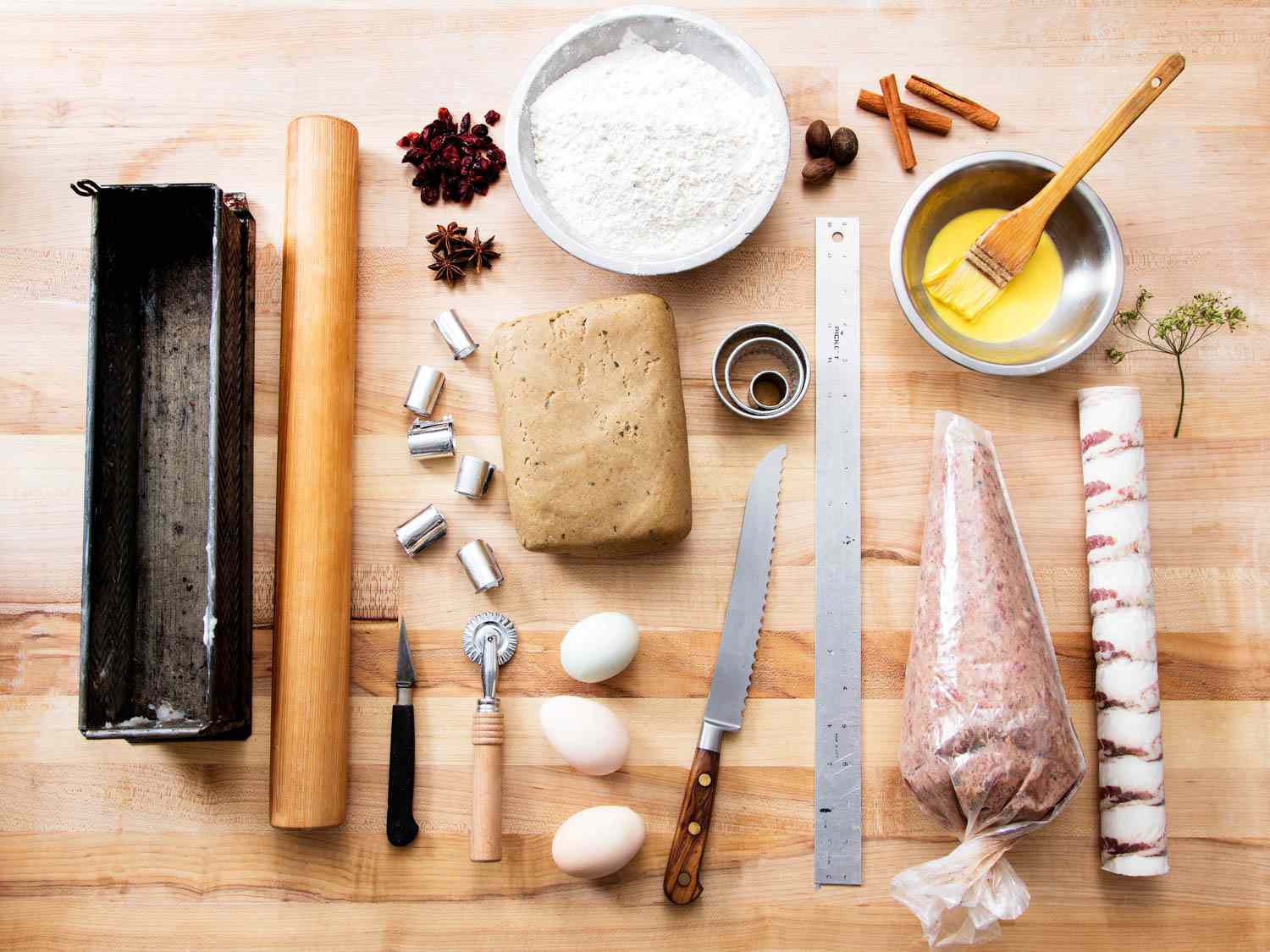 Overhead view of a wooden work table crowded with the tools and ingredients needed to make a pâté en croûte.