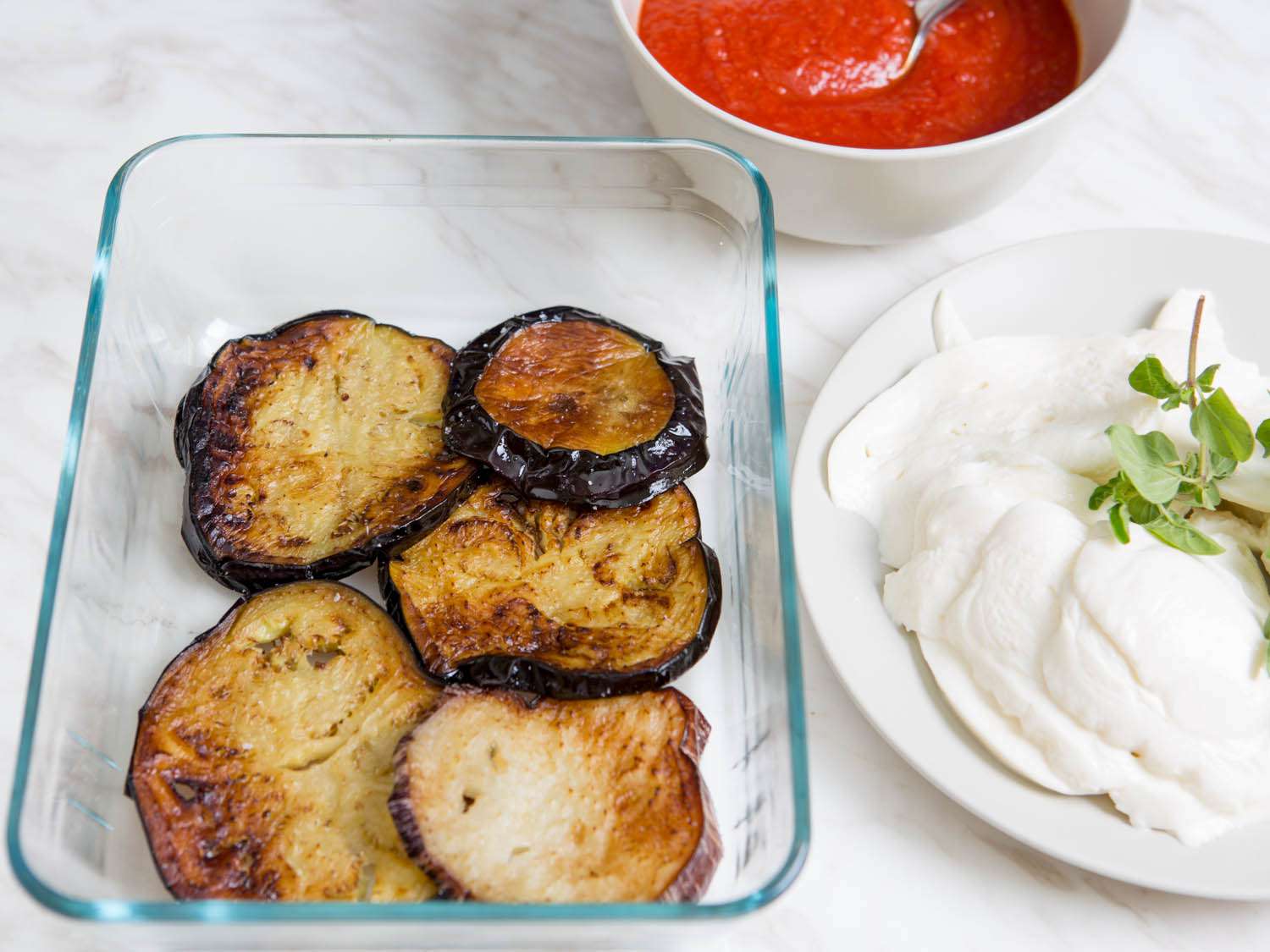 Layering slices of fried eggplant and fresh mozzarella in a baking dish.