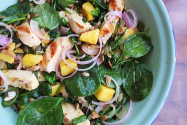 Overhead closeup of grilled chicken and spinach salad with honey mustard, served in a blue bowl.