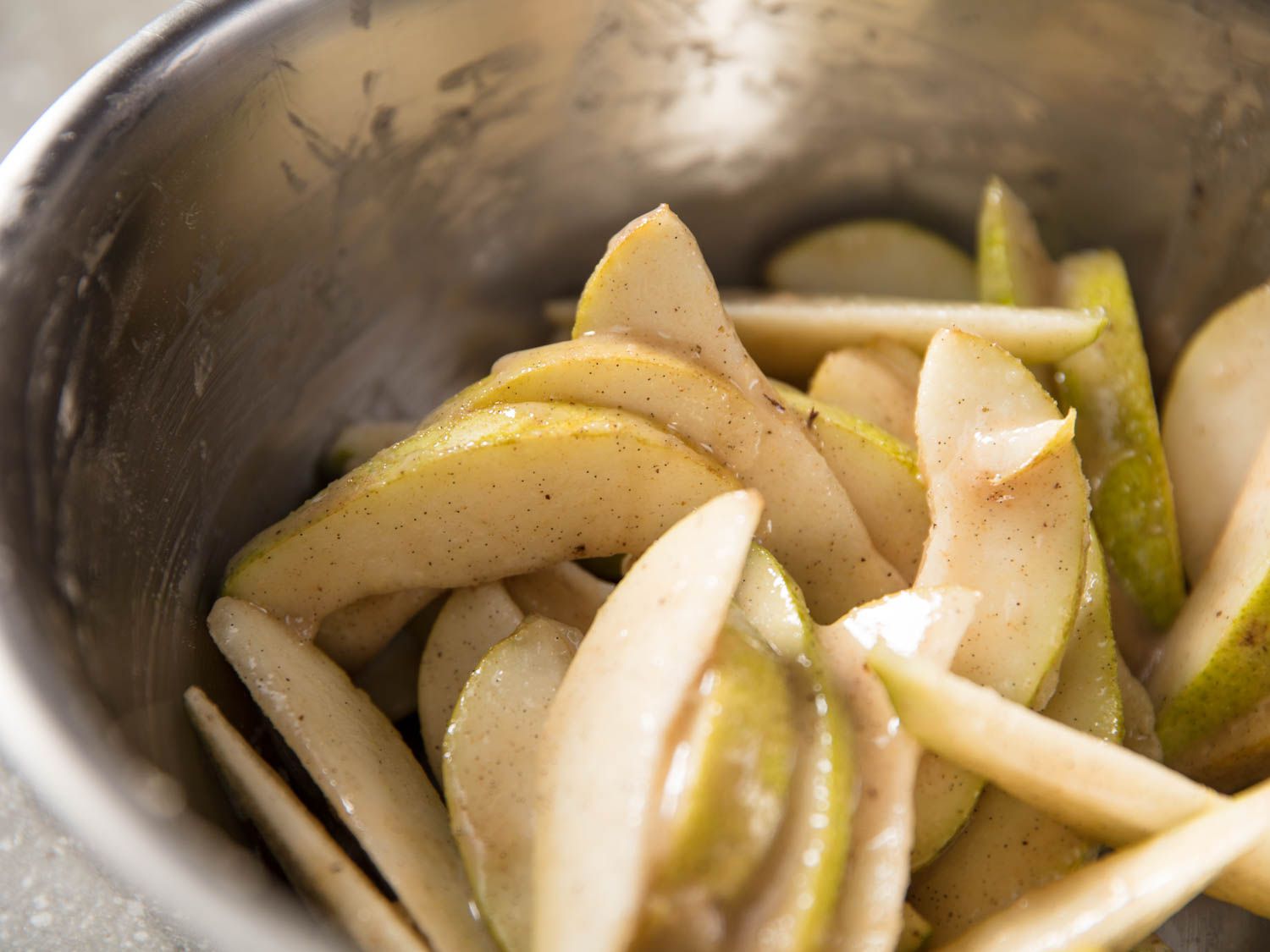 The sliced pears are tossed in a mixing bowl with sugar, spices, and vinegar.