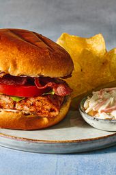 Grilled blackened-fish sandwich on a plate with potato chips, creamy coleslaw, and a pickle spear