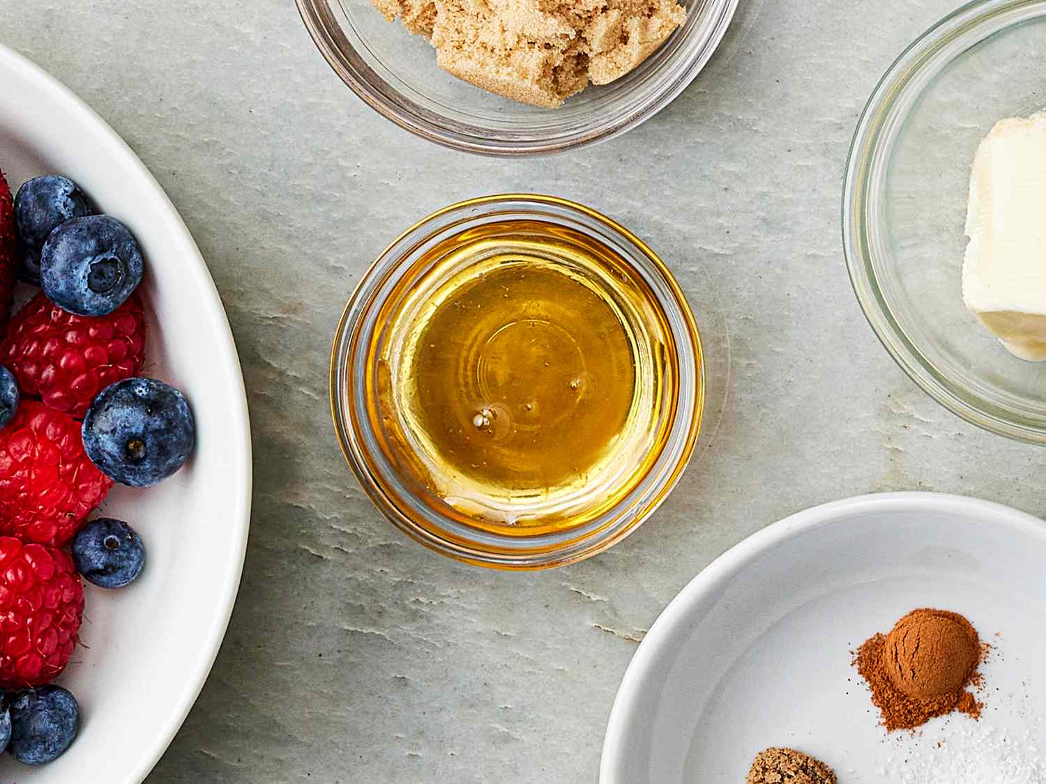 Ingredients for a recipe including honey in a small bowl berries sugar butter and spices arranged on a tabletop