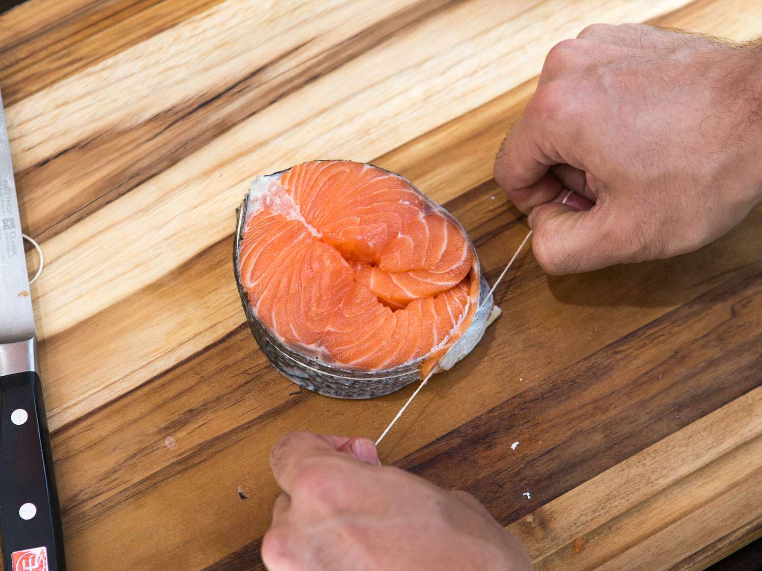 Tying up a salmon steak with butcher's twine, pulling the knot tightly.