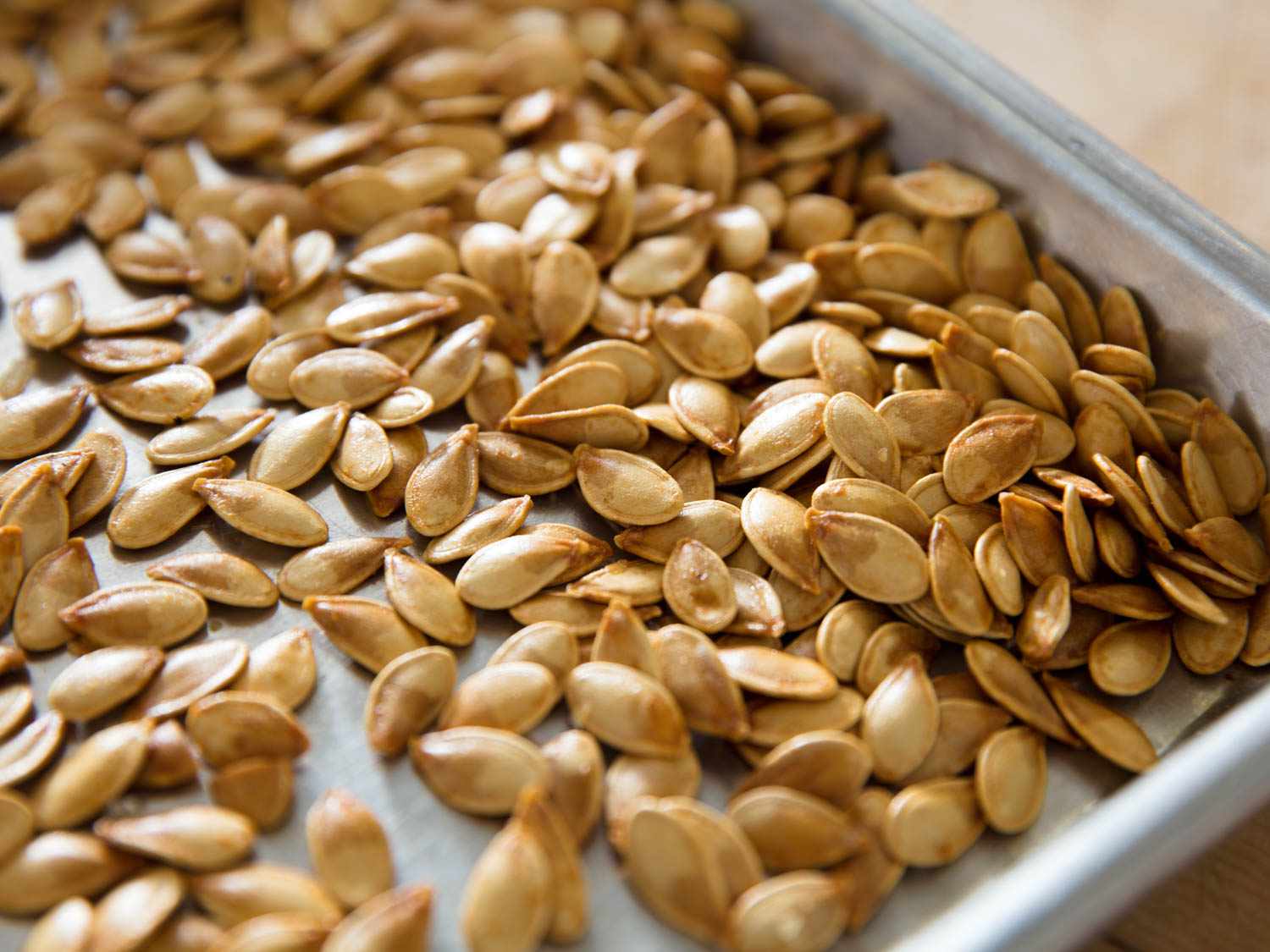 Closeup of roasted pumpkin seeds on a rimmed baking sheet.
