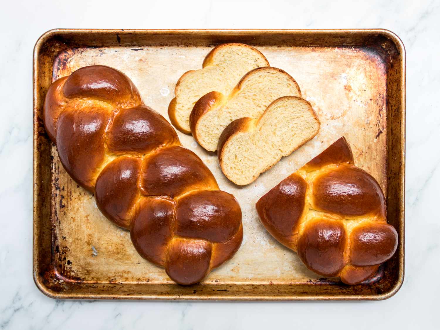 Two loaves of challah on a sheet pan. One is half sliced, the other is whole. 