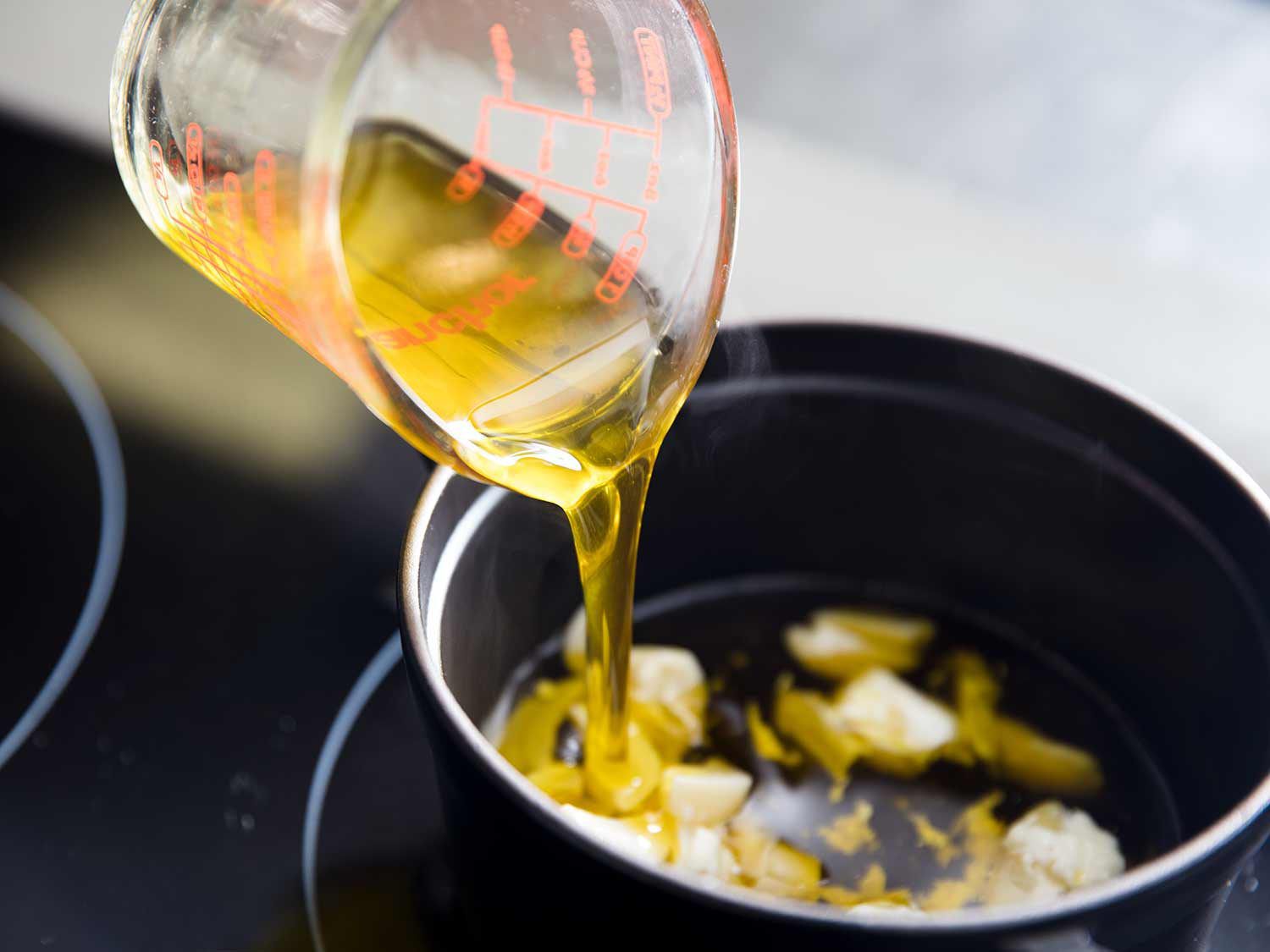 Adding olive oil to garlic cloves for garlic confit.