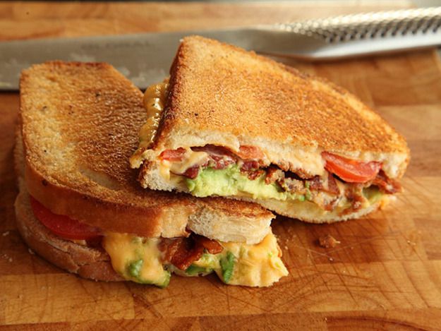  A halved Grilled Cheese With Bacon, Tomato, and Avocado, shingled on a cutting board.