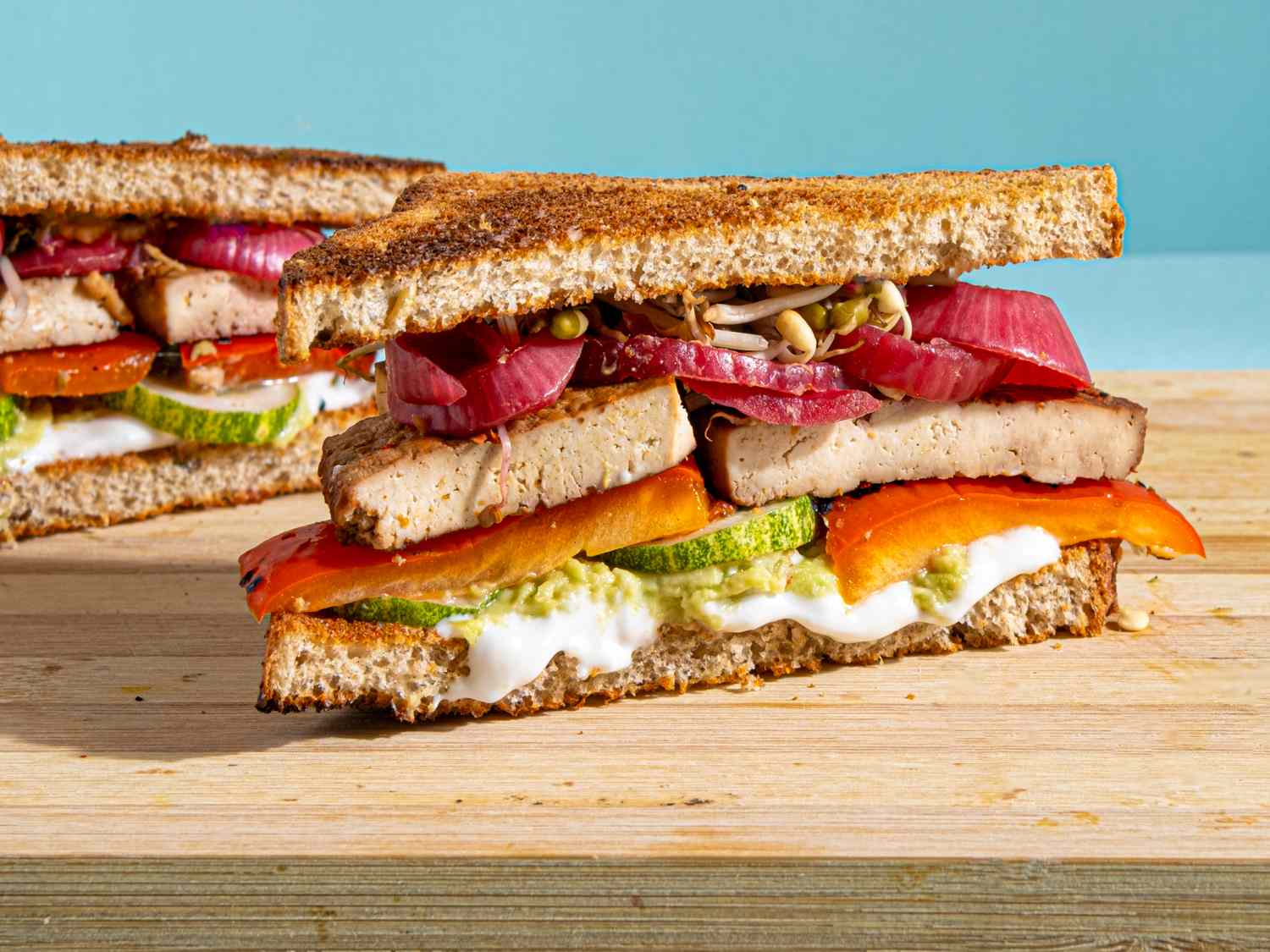 A marinated tofu sandwich layered with vegetables and spread on whole grain bread