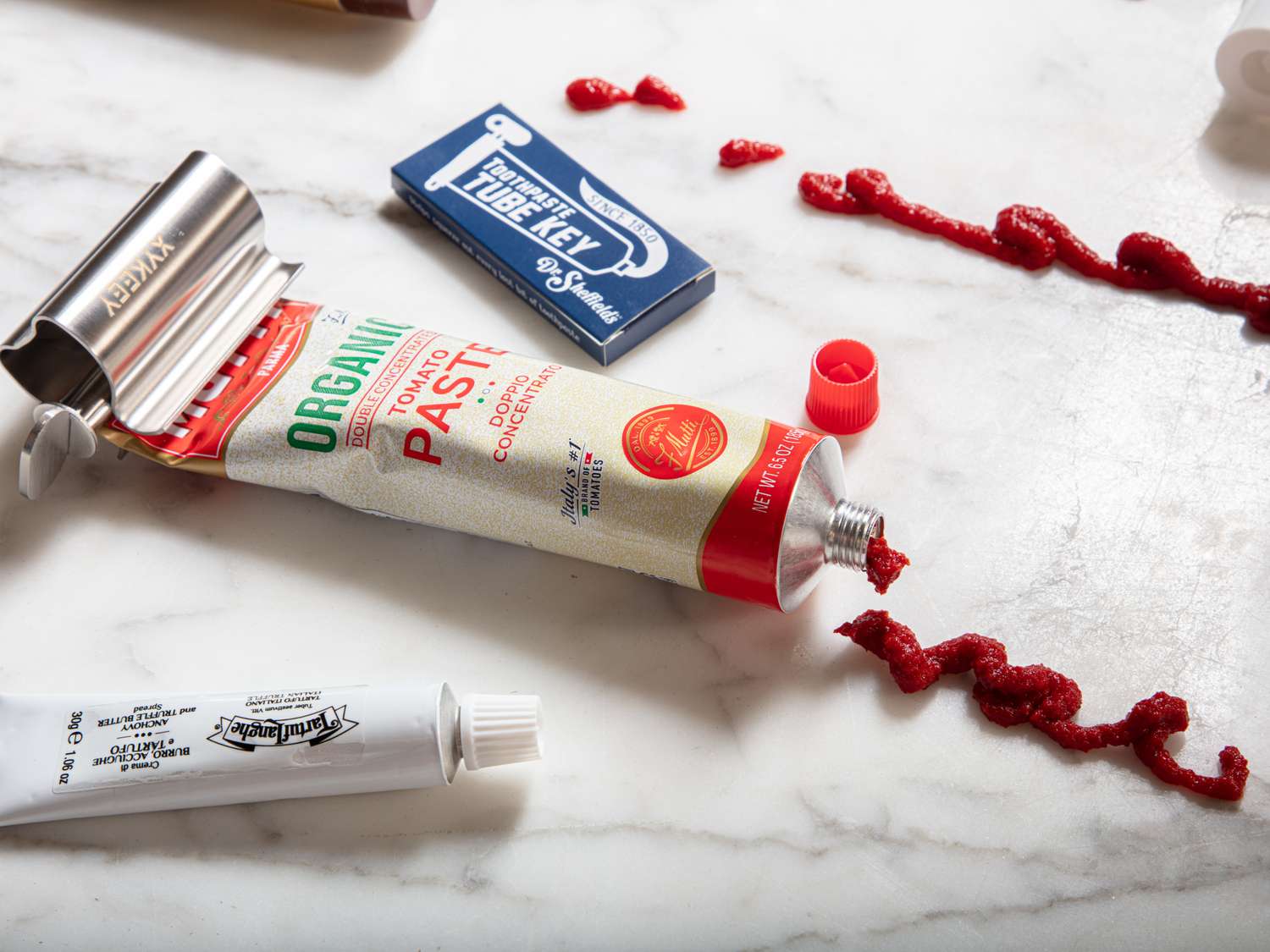 A tube of tomato paste partially squeezed using a tube squeezer with the paste spilled onto a countertop