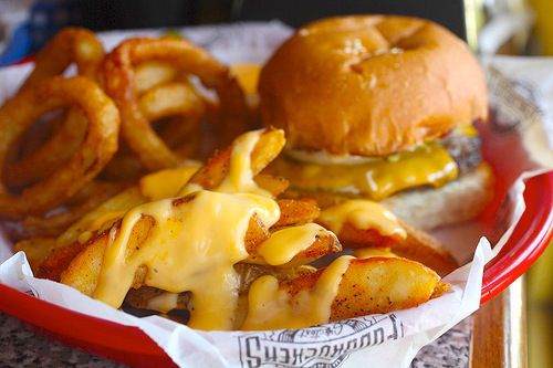 A burger, onion rings, and cheese-sauce coated french fries in a basket at Fuddruckers.