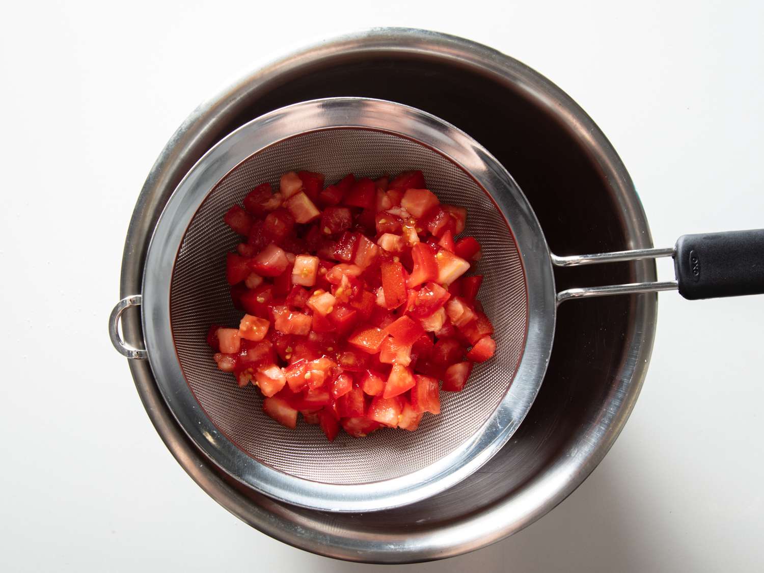 chopped tomatoes seasoned with salt in a fine mesh strainer over a bowl to release excess liquid