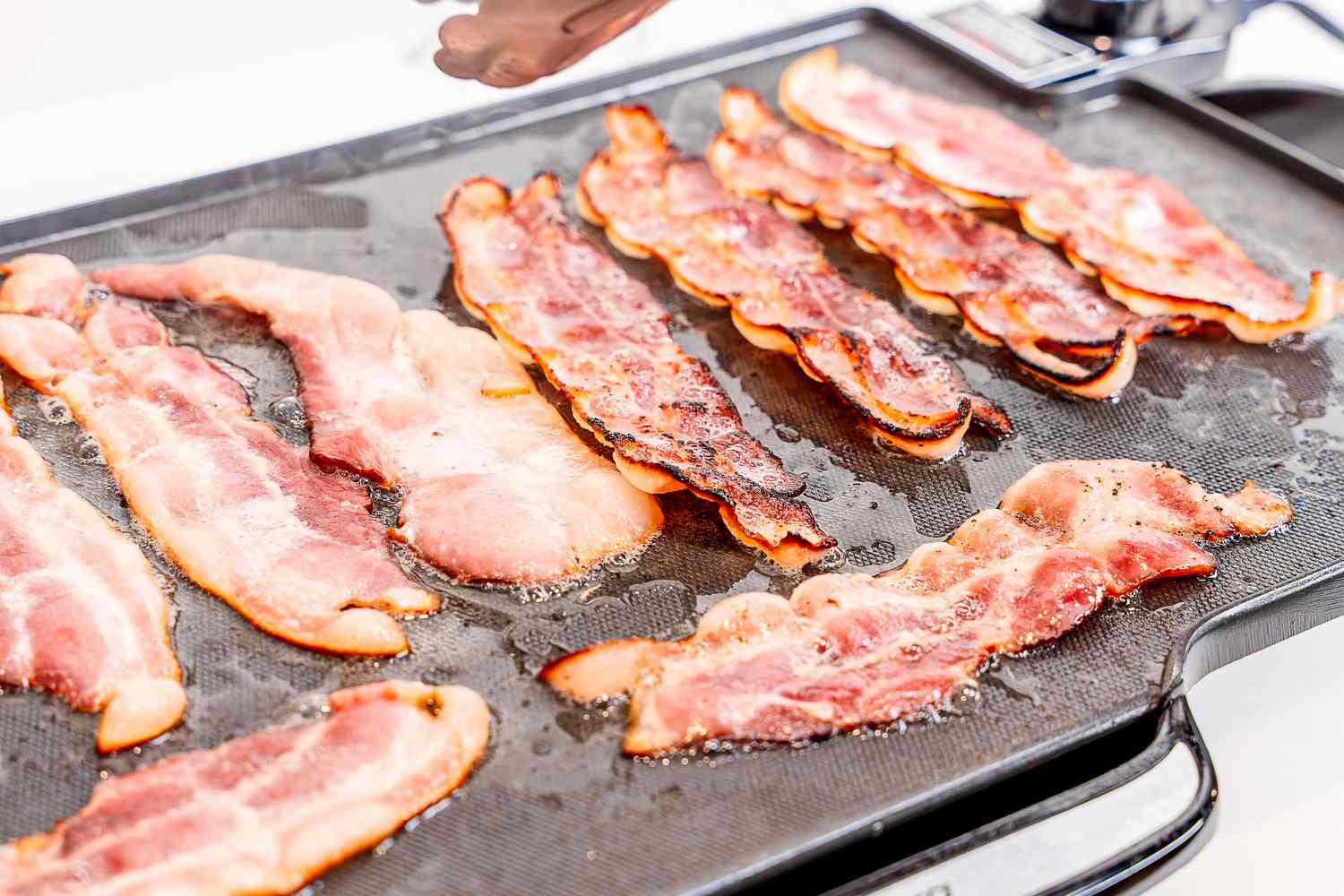 Crispy bacon cooking on an electric griddle