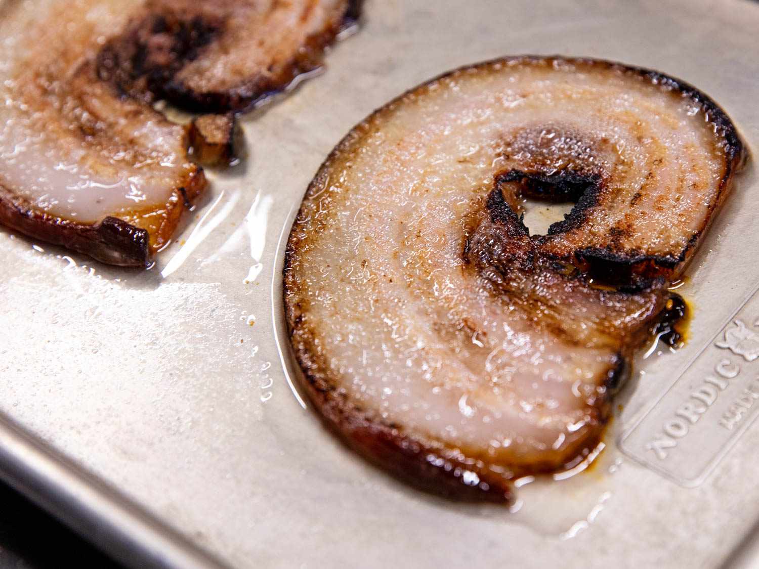 Slices of cooked and broiled pork belly on a rimmed baking sheet