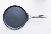 the le creuset crepe pan on a white surface