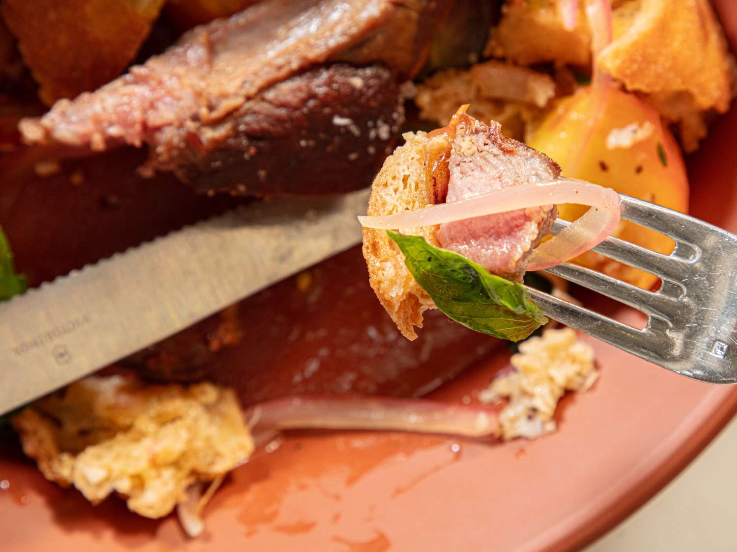 Fork holding a piece of meat and bread over a salad with a knife on a plate