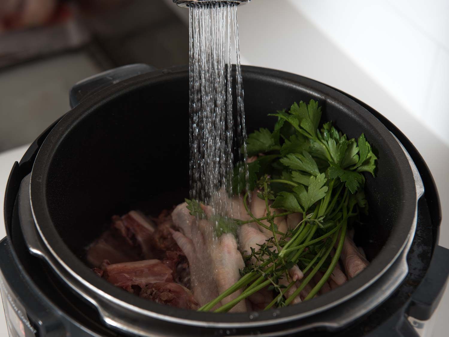 Filling a multi-cooker with water and ingredients for chicken stock.