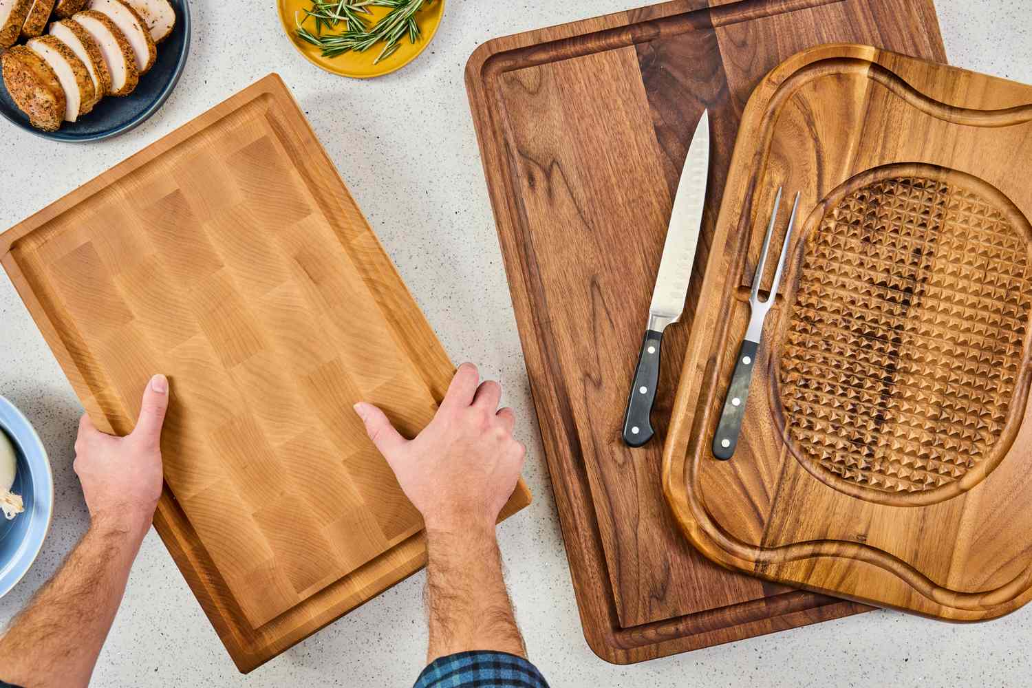 Various wooden carving boards displayed on a table with a persons hands handling one of them accompanied by a plate of food