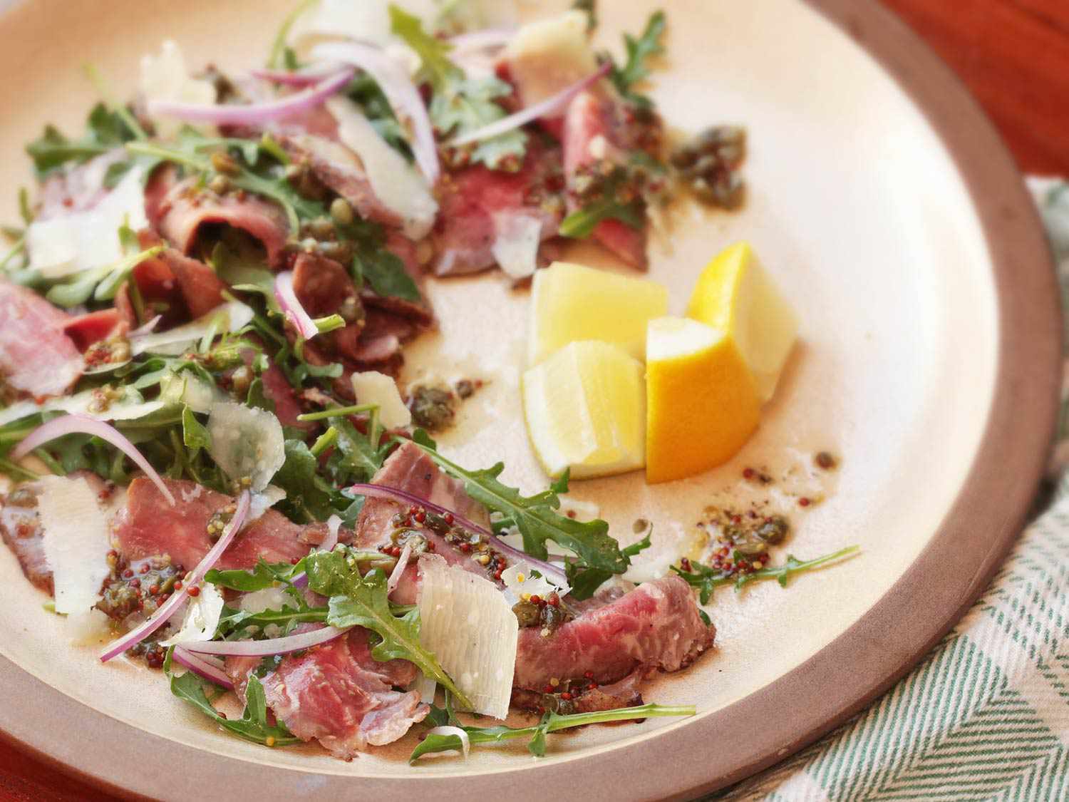 Closeup of steak carpaccio salad, served with a quartered lemon half.