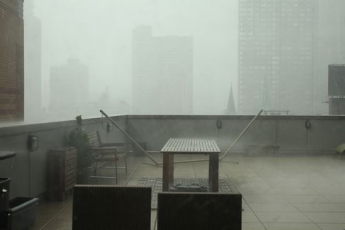 A New York City rooftop in the rain with a picnic table and chairs.