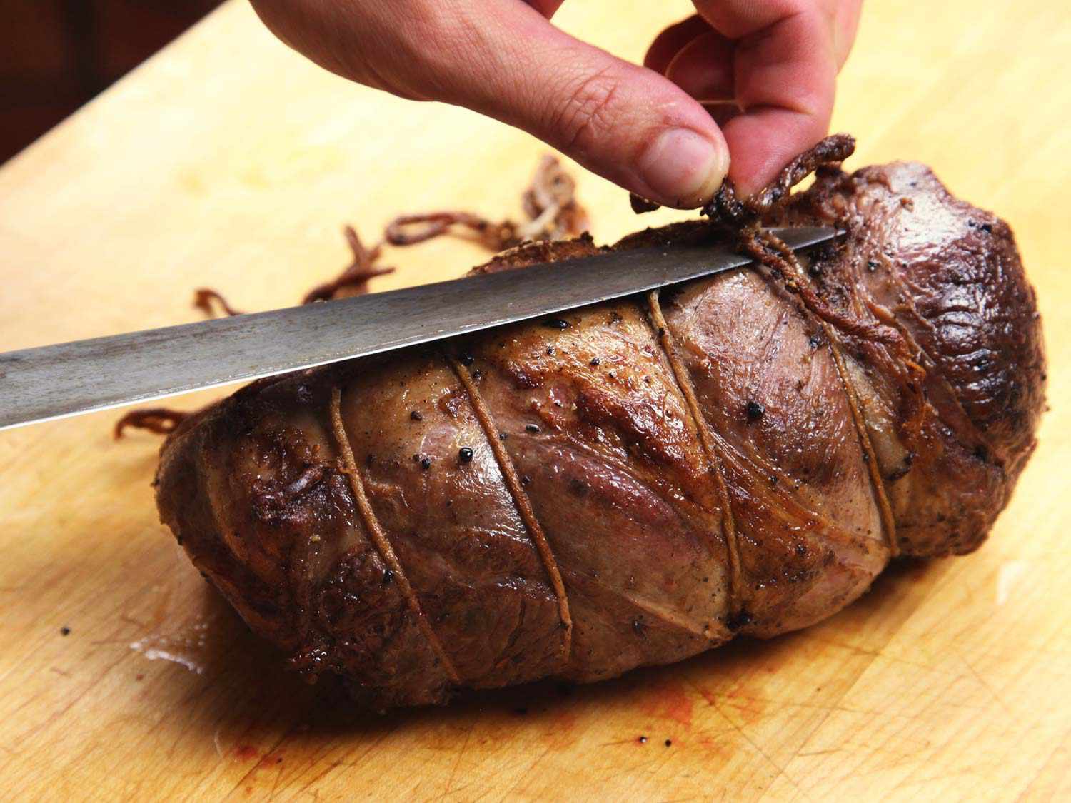 Severing twine binding roasted lamb leg with a knife