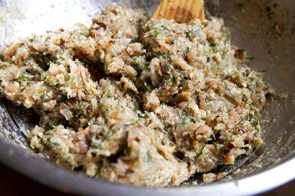 A wooden spoon mixing ground chicken with seasonings and dill in a metal bowl