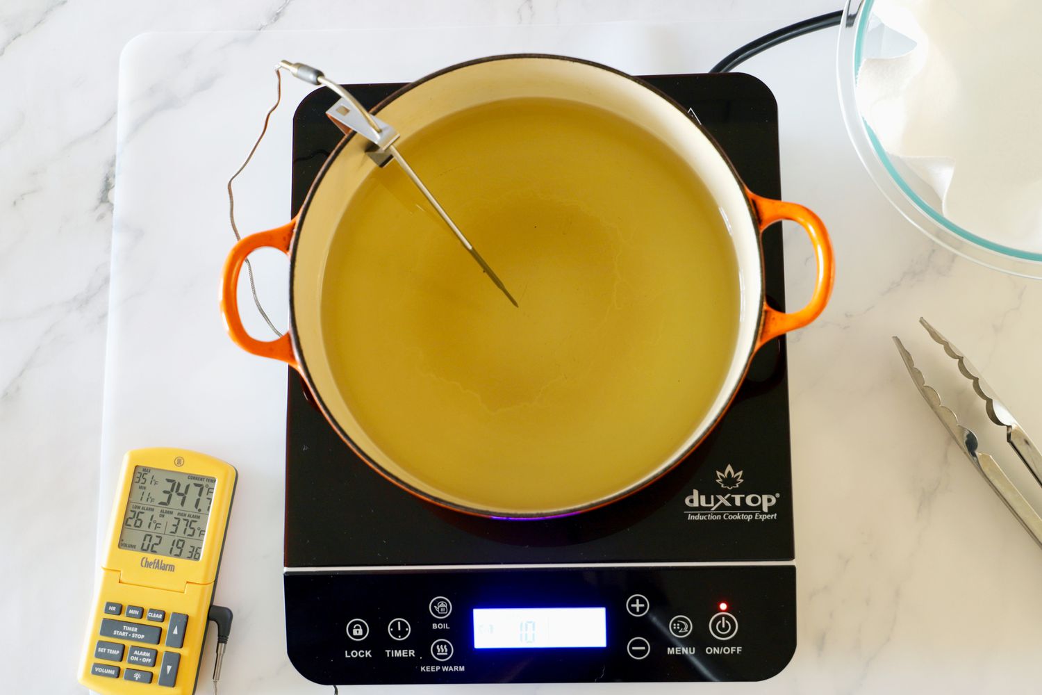 Oil heating in a Dutch oven on an induction cooktop. An instant-read thermometer is monitoring temperature.