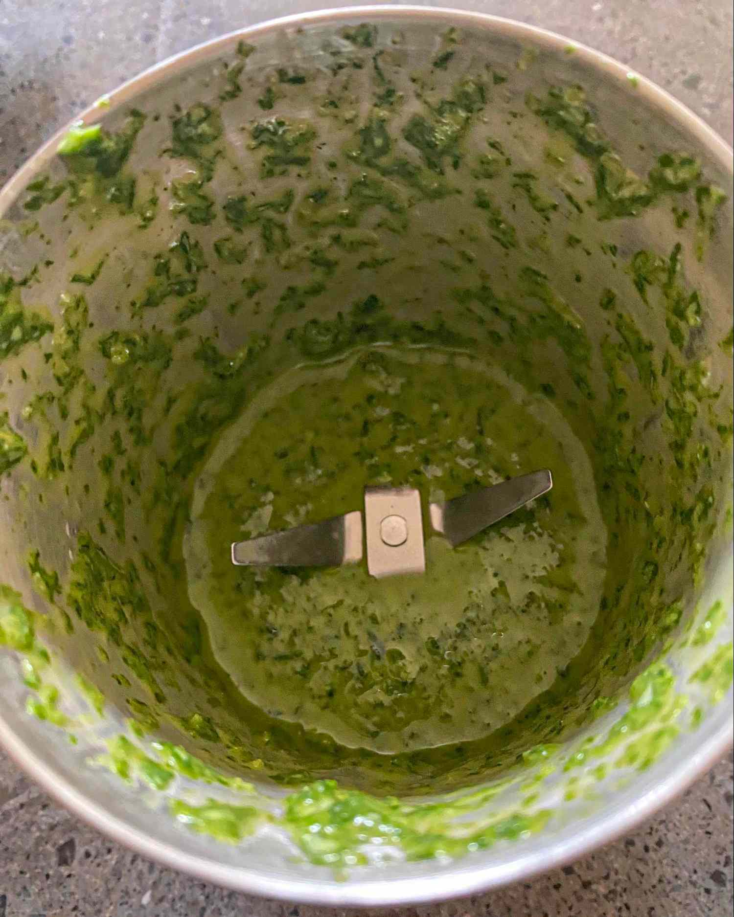 A food processor containing green pesto with visible blades