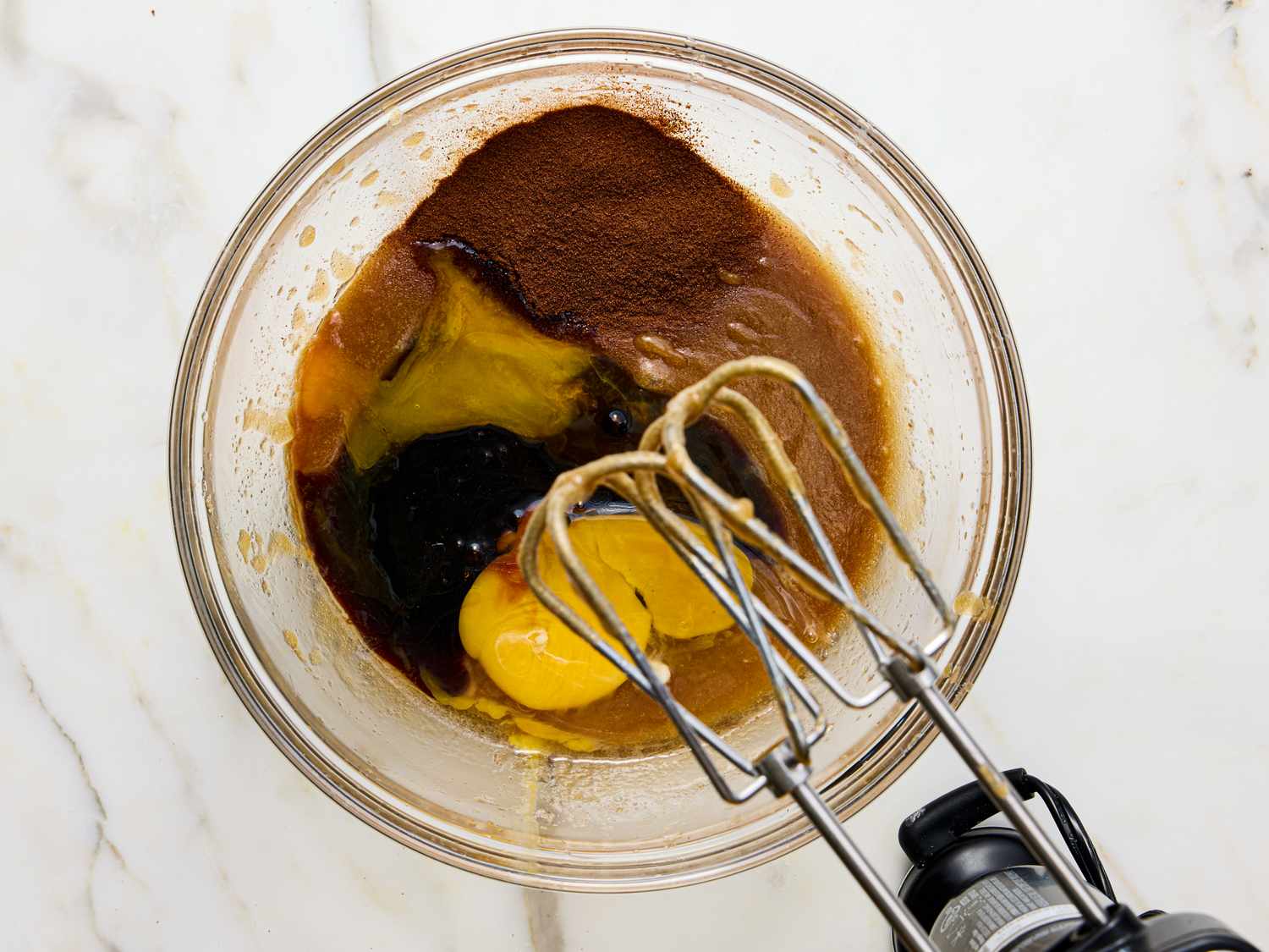 Ingredients including eggs and cocoa powder in a bowl with an electric mixer beater