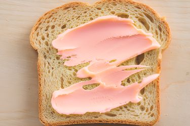 A slice of bread with pink spread on a light surface