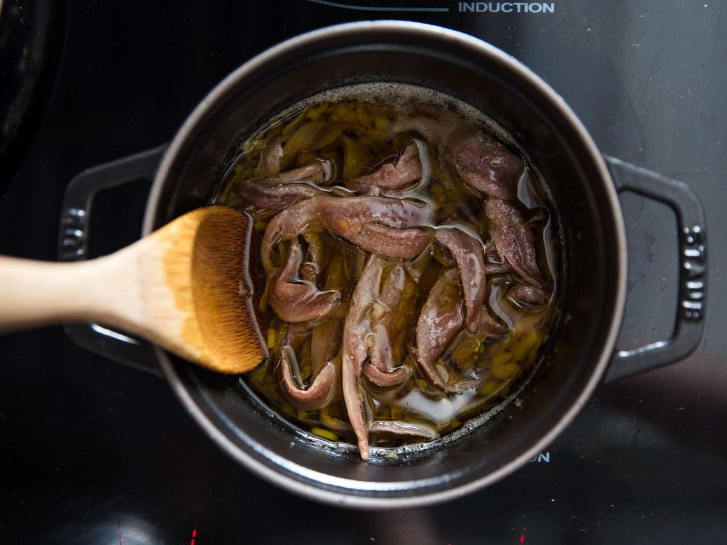 A wooden spoon stirring a pot of anchovies floating in olive oil. 
