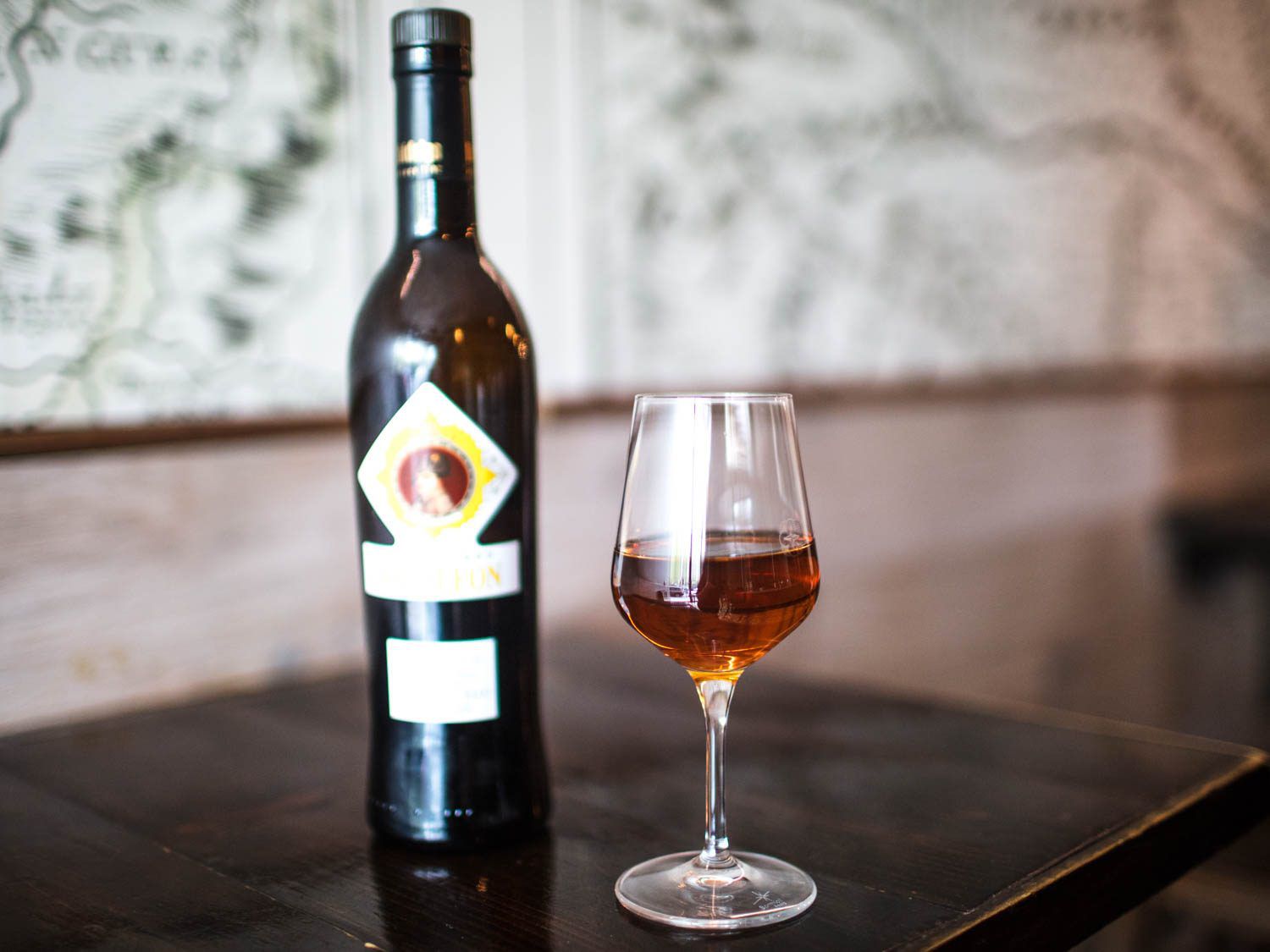 A bottle of Amontillado next to a wineglass of reddish-gold sherry on a wooden table