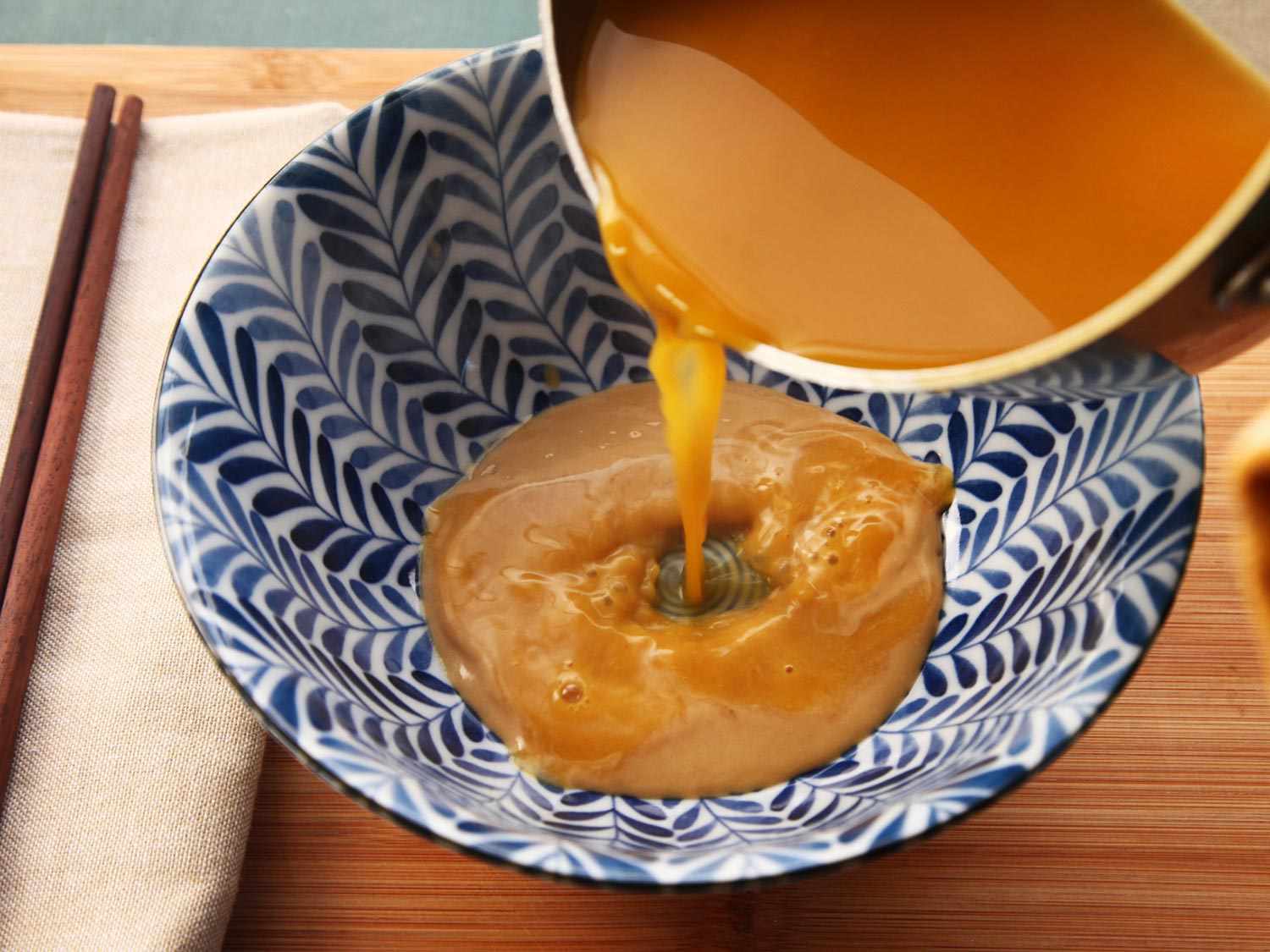 Vegan ramen broth being poured into a blue and white bowl.
