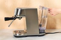 Hand attaching filled water tank from Breville Bambino Plus Espresso Machine on white countertop