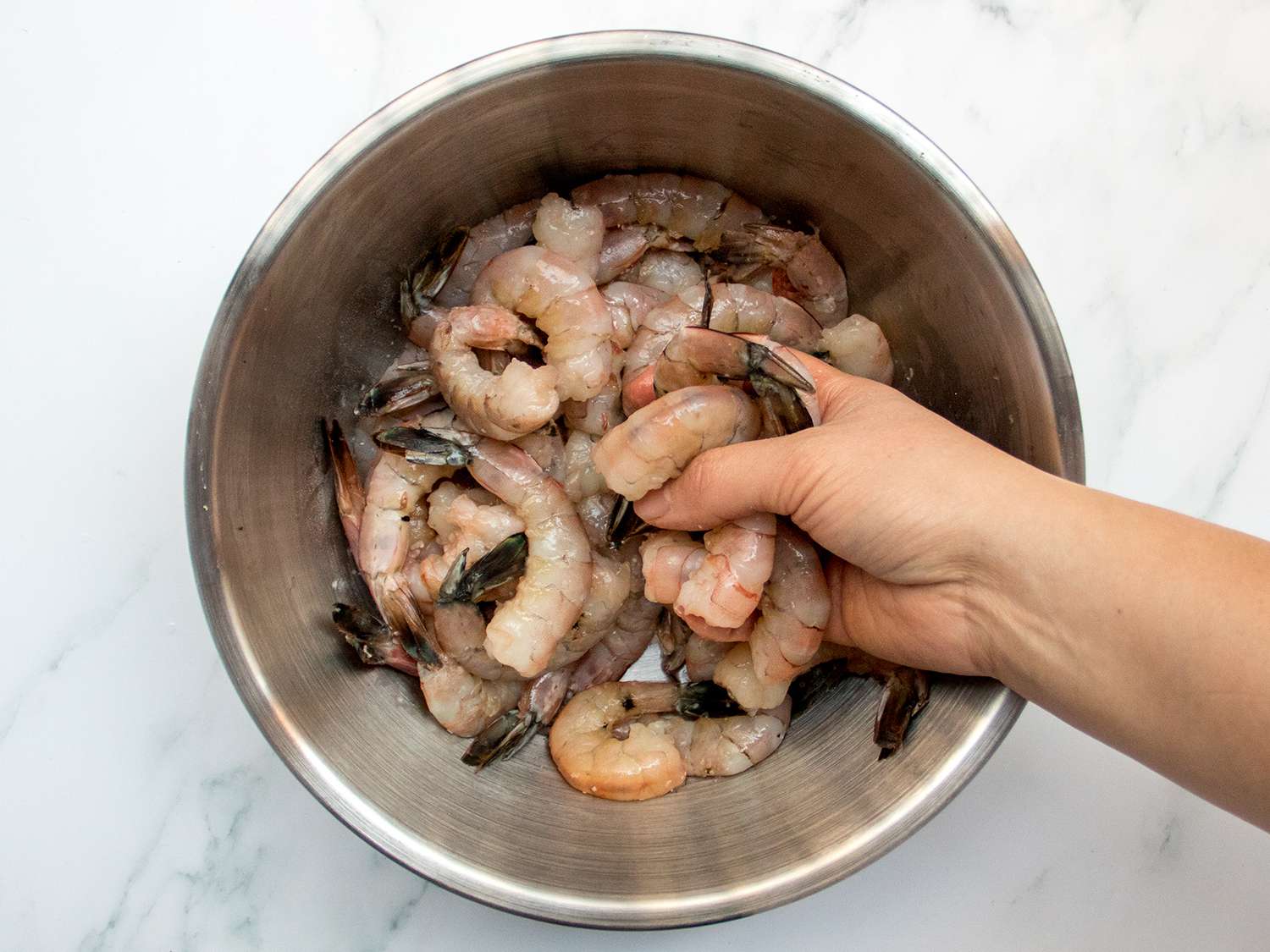 Raw shrimp being mixed in a metal bowl by a hand.